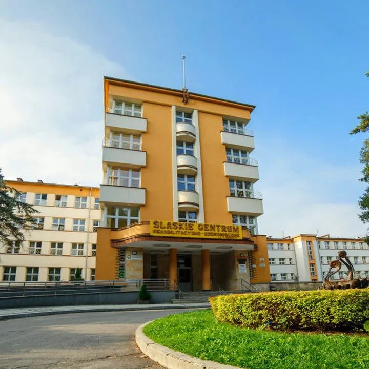 Budynek Śląskiego Centrum Rehabilitacyjno-Uzdrowiskowego w słoneczny dzień, otoczony zielenią.